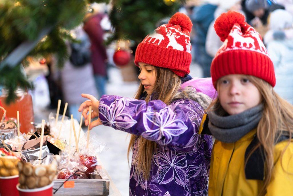 Two children in winter clothes choose homemade sweets at the Christmas market.